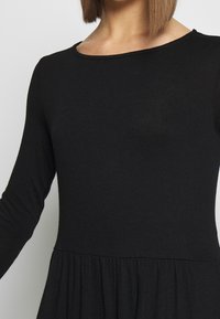 Svart långärmad klänning med rund halsringning. Tillverkad av mjukt och stretchigt tyg, med en gatherad utsvängd kjol och slät textur.