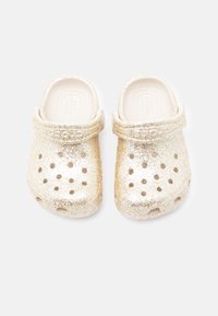 Γυαλιστερά χρυσά ξυλοπάπουτσα κατασκευασμένα από ελαφρύ υλικό με οπές αερισμού και λουράκι στο πίσω μέρος για σταθερή εφαρμογή. Λείο, στρογγυλεμένο σχέδιο.