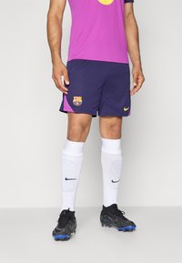 Violetinė ir tamsiai mėlyna Barcos futbolo apranga su logotipu, derinama su baltais porceliano kojiniais ir juodais batais su mėlynomis akcentais. Lygus, kvėpuojantis audinys.