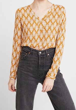 Long-sleeve top featuring an orange background with white leaf patterns, V-neck design, paired with high-waisted black jeans.