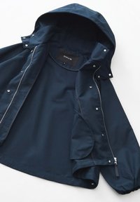 Marineblauwe, lichte regenjas met een capuchon, rits aan de voorkant, drukknopen en zijzakken. Glad materiaal met een matte afwerking. Merklabel zichtbaar.