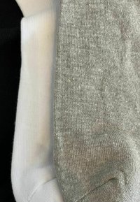 Drei Paar Socken in Grau, Weiß und Schwarz. Die graue Socke hat eine strukturierte Oberfläche, während die weißen und schwarzen Socken eine glatte Oberfläche haben.