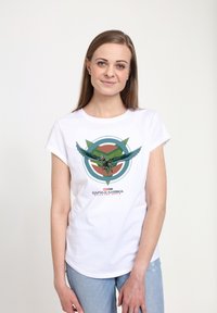 Camiseta de algodón blanca con un estampado gráfico de un personaje con alas, centrado en un diseño circular en verde, rojo y azul, con texto abajo.