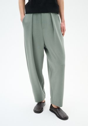 Pantaloni larghi verde chiaro con pieghe, realizzati in tessuto morbido. Abbinati a scarpe slip-on nere, adatti per un look casual.