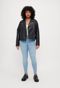 Black leather biker jacket with silver zippers, collar, and long sleeves. Paired with light blue skinny jeans and platform shoes.