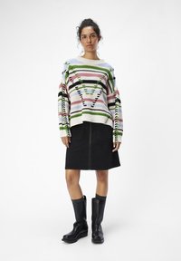 Suéter de punto multicolor con un patrón geométrico, combinado con una falda de mezclilla negra. Botas de cuero negras hasta la rodilla completan el atuendo.