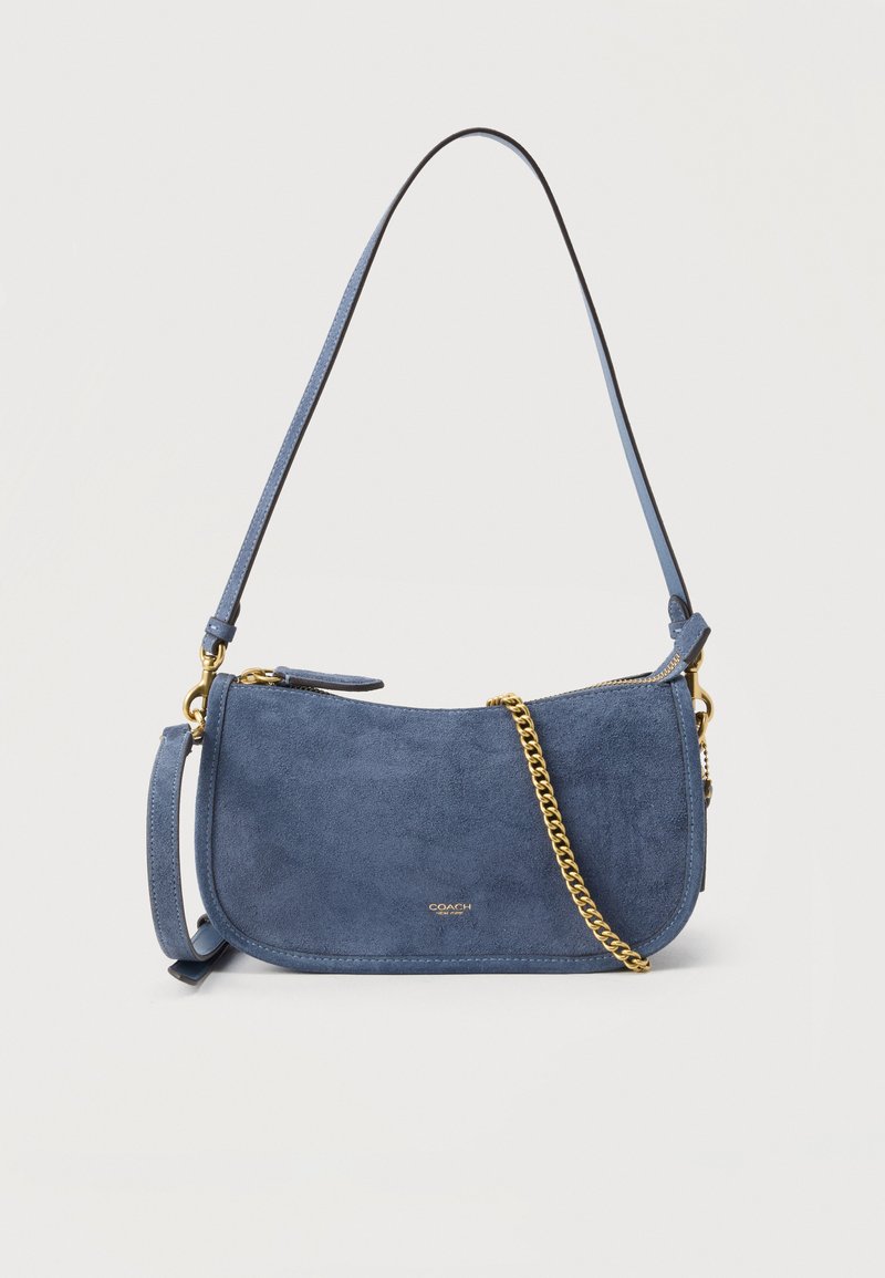 Τσάντα Coach από μπλε σουέντ με λεπτομέρειες από χρυσή αλυσίδα, μονή λουρί ώμου και κλείσιμο με φερμουάρ, παρουσιάζεται μπροστά σε ανοιχτό φόντο.