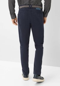 Marineblauwe katoenen chinos met een slanke pasvorm, voorzien van een rechte pijp, achterzakken en een gestructureerde grijze ceintuur. Draagt bij donkere schoenen.
