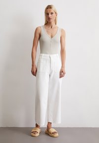 Beige mouwloze bodysuit met een V-hals en knoopdetail; gecombineerd met hoge taille witte wijde jeans en geweven platformsandalen.