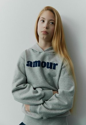 Grå sweatshirt med marineblå "amour" tekst. Den har hætte og lange ærmer, med en afslappet pasform og blød tekstur.