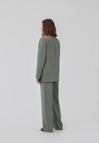 Olivengrønn skreddersydd drakt med en strukturert blazer og vide bukser. Rene linjer med minimal detaljering, glatt tekstur.