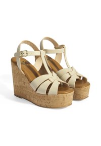 Hakken sandalen met een kurken plateau en crèmekleurige leren banden. Voorzien van een open teen, T-band ontwerp en een verstelbare enkelgesp.
