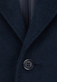 Granatowy wełniany płaszcz z zapięciem na guziki, wyraźnym kołnierzem i ukrytą kieszenią na zamek. Teksturowana tkanina z gładkim wykończeniem.