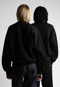 Felpe nere con vestibilità rilassata, dotate di polsini e orli a costine, indossate sopra jeans in denim scuri, viste da dietro.