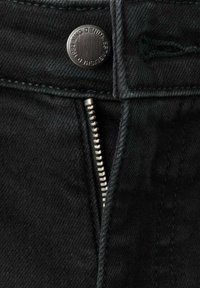 Jean en denim noir avec un bouton argenté, une braguette zippée à dents métalliques, et des coutures foncées le long des coutures. Détail du tissu texturé visible.