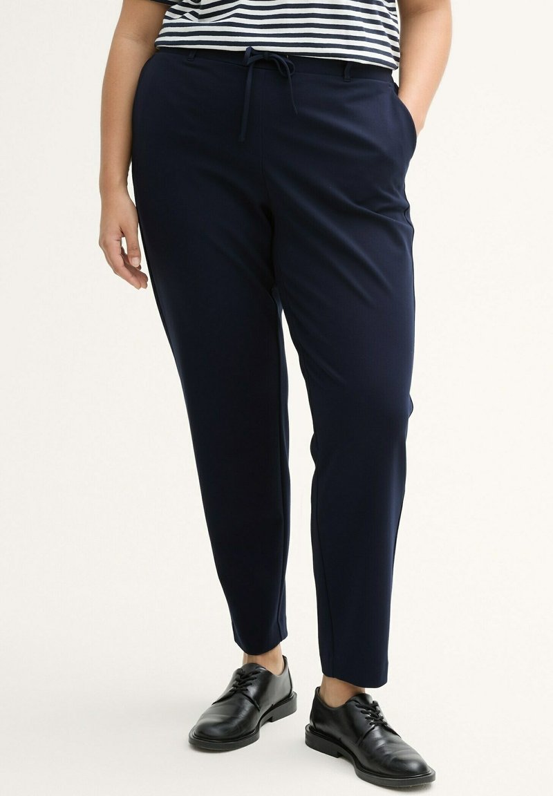 Pantalones azul marino confeccionados en una tela lisa, con una cintura con cordón y piernas ajustadas. Combinados con zapatos negros de cordones.