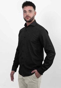 Zwarte button-up blouse gemaakt van een gestructureerde stof, met een kraag, lange mouwen en een slim fit, gecombineerd met lichtgekleurde broeken.