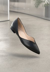 Black leather flat shoe with a pointed toe, low heel, and a v-shaped cut at the front. The interior is beige with subtle branding.