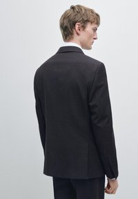 Giacca da completo marrone scuro su misura, tessuto strutturato, spacco singolo sul retro, chiusura con due bottoni e rever a lancia.