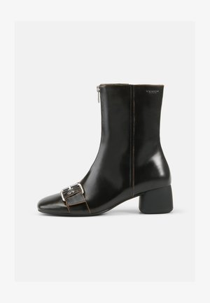 Bota de cano curto em couro preto com bico arredondado, fecho lateral com zipper e detalhe de fivela prateada. Apresenta um salto robusto e costura em contraste.