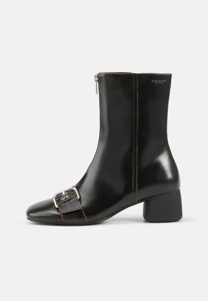 Μαύρη δερμάτινη μπότα αστραγάλου με στρογγυλή μύτη, φερμουάρ στο πλάι και ασημένια λεπτομέρεια από πόρπη. Διαθέτει χοντρό τακούνι και αντίθετη ραφή.