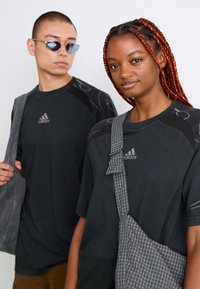 Black athletic t-shirts with gray accents, one featuring a checked bag strap. Both wear sunglasses; the background is a plain white.