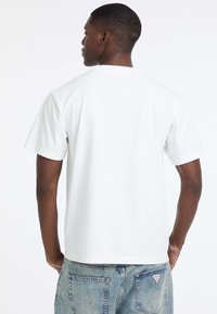 Biała bawełniana koszulka z krótkim rękawem i okrągłym dekoltem. Gładka tekstura i luźny krój, w połączeniu z niebieskimi dżinsami.