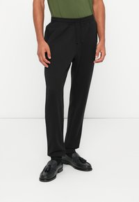 Sorte sweatpants laget av mykt stoff med snor i midjen, sidelommer og rett ben-design, paret med sorte loafers.