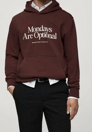Persona que lleva una sudadera con capucha color granate con los textos "Los lunes son opcionales" y "¿Lunes? Nunca lo he oído", combinada con pantalones negros y una camisa blanca.