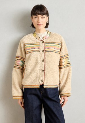 Beige fleece jacket with multicolored horizontal stripes, oversized fit, and button closure. Features vibrant embroidery on sleeves and pockets.