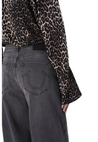 Luipaardprint blouse met lange mouwen, gecombineerd met grijze denim jeans voorzien van opvallende stiksel op de achterzakken. Zwarte tailleband detail.