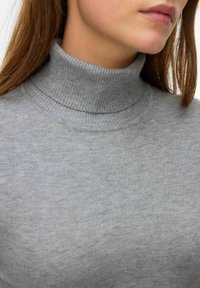 Siv pulover s turtleneck ovratnikom, izdelan iz mehkega, rebrastega pletenega materiala. Oblikovanje vključuje visok ovratnik in gladko teksturo z minimalnimi detajli.