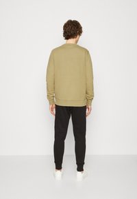 Felpa khaki con maniche lunghe e polsini a coste, abbinata a pantaloni jogger neri e scarpe da ginnastica bianche, vista da dietro.