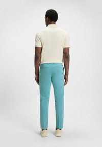 Jasno beżowa koszulka polo i turkusowe spodnie slim fit z bocznymi kieszeniami oraz dopasowanym krojem; gładka tekstura, swobodny wygląd.