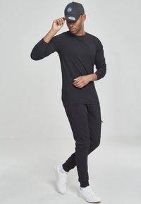 Fekete hosszú ujjú ing és fekete slim fit melegítőnadrág, sötét sapkával, amelyen a NASA logó található, valamint fehér sportcipővel párosítva.