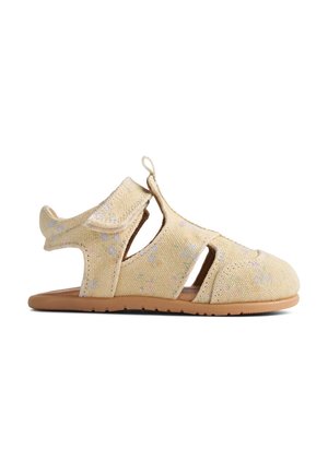 Beżowy sandał dla małego dziecka z kwiatowym wzorem, otwartymi bokami, regulowanymi paskami na rzep oraz elastyczną brązową podeszwą.