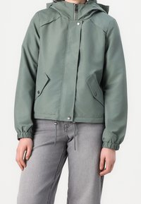 Grüne wasserdichte Jacke mit Kapuze, Frontreißverschluss, Druckknöpfen, elastischen Bündchen und zwei Seitentaschen. Glatte Textur mit tailliertem Schnitt.