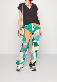 Top de punto oscuro de manga corta combinado con pantalones anchos de patrón abstracto multicolor. Un bolso plateado y zapatillas deportivas completan el conjunto.
