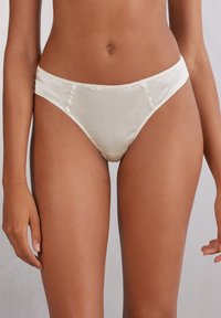 Kremowe satynowe figi w bikini o gładkiej fakturze, niskim stanie i minimalnych szwach, które zapewniają elegancki wygląd.