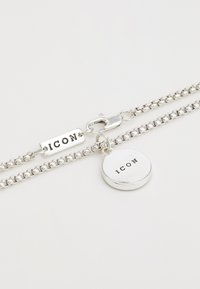 Bracelet en chaîne en argent avec un fermoir, un charme rectangulaire plat et un charme rond, tous deux gravés avec "ICON." Texture lisse et finition polie.