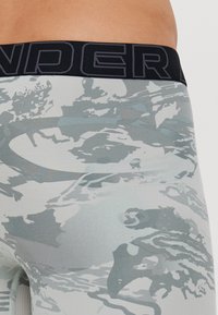 Leggings cu un model gri și alb, cu o talie neagră pe care este inscripționat textul "UNDER". Materialul pare neted, cu un ușor luciu.