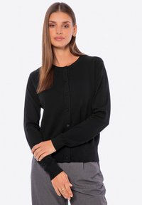 Cardigan nero con scollo tondo, maniche lunghe e chiusura con bottoni. Realizzato in un tessuto liscio con un design aderente. Dettagli ai polsini.