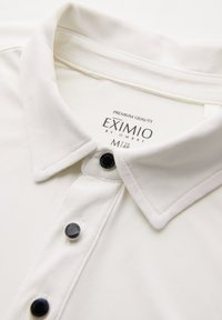 Bílá košile s černými knoflíky a štítkem "EXIMIO by OMBRE", velikost M, viditelný uvnitř límce.