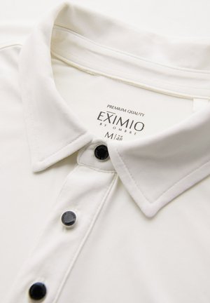 Valkoinen kauluspaita mustilla napilla ja "EXIMIO by OMBRE" -tunnus, koko M, näkyvissä kauluksen sisäpuolella.