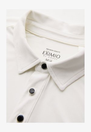 Valkoinen kauluspaita mustilla napilla ja "EXIMIO by OMBRE" -tunnus, koko M, näkyvissä kauluksen sisäpuolella.