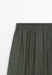 Jupe verte foncée en tissu texturé et froissé. Dotée d'une taille élastique et d'une silhouette fluide avec des détails plissés.