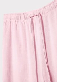 Pantalon en tissu rose clair avec une ceinture élastique et un cordon ajustable assorti sur le côté droit.