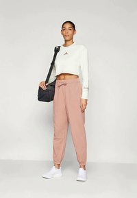Sweatshirt branca cropped com logótipo rosa, combinada com calças de moletão largas rosa e ténis brancos. Uma mala preta de ombro é usada no lado.