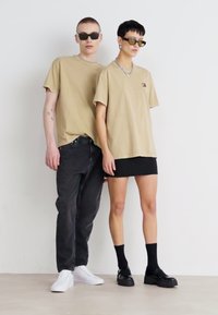 Beige ylisuuria T-paitoja kahdella mallilla, yhdistettynä mustiin farkkuihin ja hameeseen, mustiin chunky-kengiin ja aurinkolaseihin. Minimalistinen muotoilu ja moderni istuvuus.