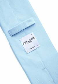 Ljusblå tygknyt med ett texturerat diagonalt mönster. Etiketten visar "JOHN HENRIC SWEDEN, Made in Italy," sytt på baksidan.